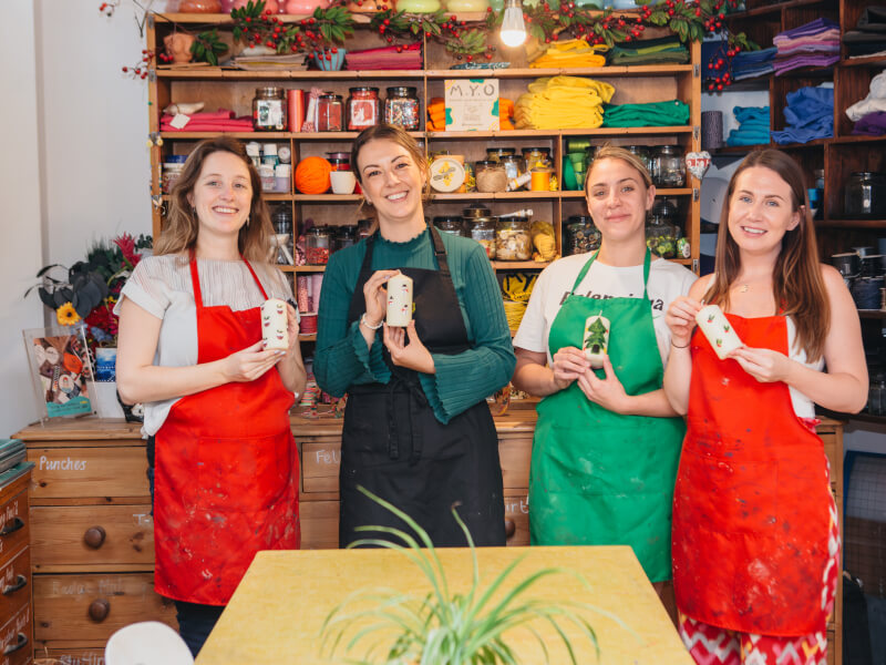 Four women in aprons holding up hand-painted candles